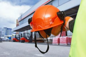An orange helmet held against a background of a job site.